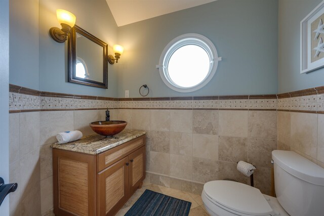 bathroom with wainscoting, toilet, tile patterned flooring, vanity, and tile walls