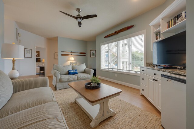 living room with baseboards, a ceiling fan, and light wood-style floors