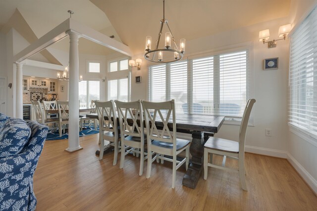 dining room with ornate columns, lofted ceiling, light wood-style flooring, and an inviting chandelier