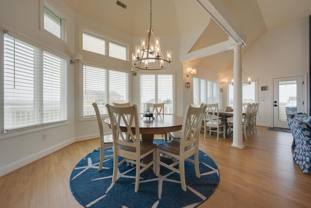 dining space featuring high vaulted ceiling, visible vents, light wood-type flooring, ornate columns, and an inviting chandelier