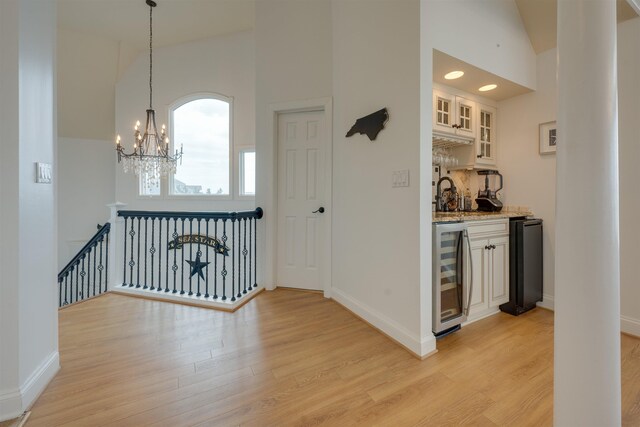 hallway featuring high vaulted ceiling, light wood-style flooring, beverage cooler, an upstairs landing, and baseboards