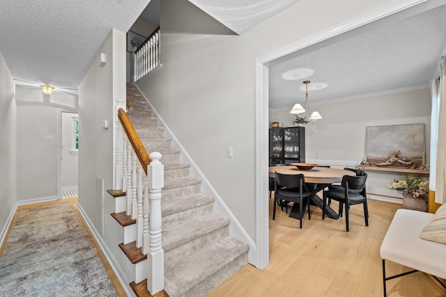 stairway with a textured ceiling, a notable chandelier, baseboards, ornamental molding, and hardwood / wood-style floors