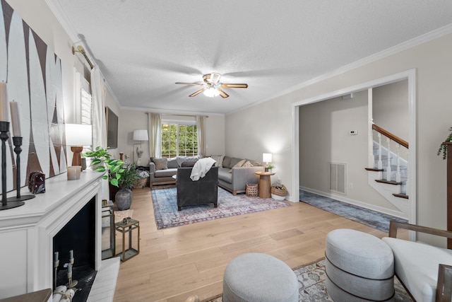 living area featuring visible vents, stairs, crown molding, a textured ceiling, and light wood-style floors