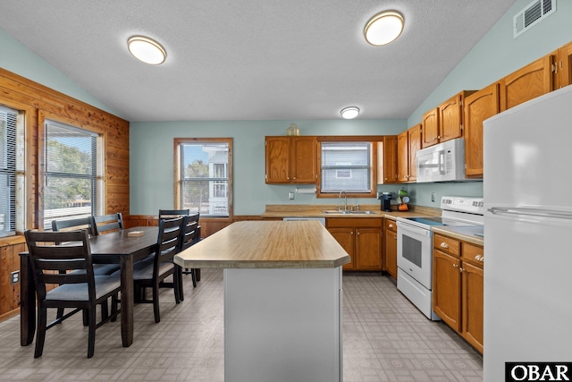 kitchen with visible vents, light floors, wood walls, white appliances, and a sink