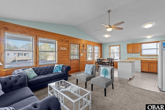 living area featuring lofted ceiling, a ceiling fan, wood walls, and light carpet