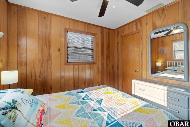 bedroom featuring visible vents, a ceiling fan, and wooden walls