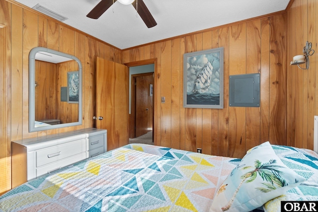 bedroom featuring a ceiling fan, visible vents, electric panel, wood walls, and crown molding