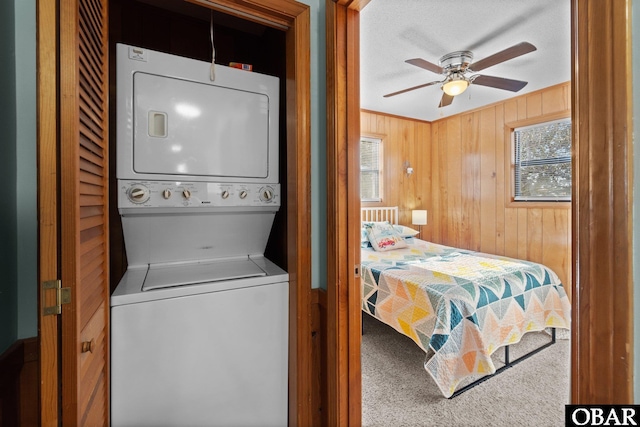 washroom with laundry area, a healthy amount of sunlight, stacked washer / drying machine, and wood walls