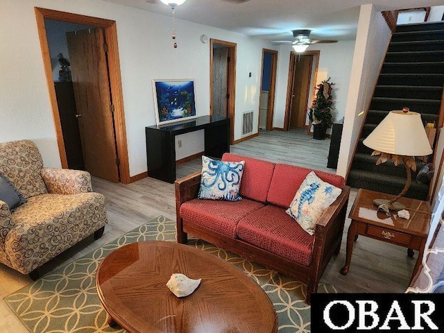 living room with visible vents, light wood-style floors, baseboards, stairs, and ceiling fan