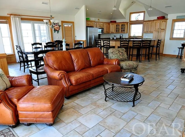 living area with visible vents, an inviting chandelier, stone finish floor, vaulted ceiling, and baseboards