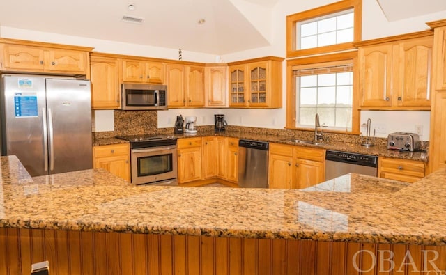 kitchen with appliances with stainless steel finishes, visible vents, glass insert cabinets, and light stone counters