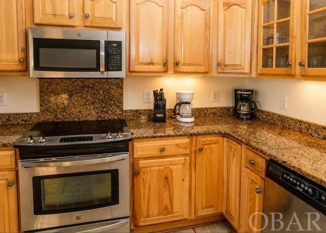 kitchen featuring stainless steel appliances, glass insert cabinets, and dark stone countertops