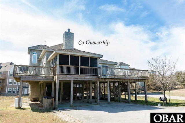 135 Ships Watch Dr Lot 32, Duck, NC 27949 - rear view of house featuring a carport, a sunroom, a wooden deck, concrete driveway, and a chimney
