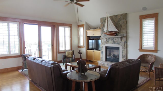 living area with light wood-type flooring, a fireplace, a wealth of natural light, and lofted ceiling