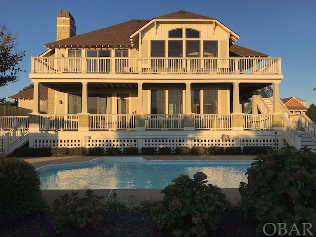 rear view of house featuring board and batten siding, a chimney, an outdoor pool, and stairway