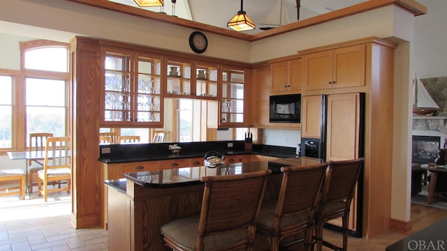 kitchen with dark countertops, hanging light fixtures, a glass covered fireplace, black microwave, and a kitchen bar