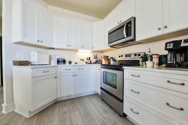 kitchen with stainless steel appliances, light countertops, white cabinetry, and wood tiled floor