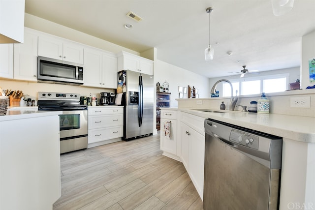 kitchen with a sink, white cabinetry, light countertops, appliances with stainless steel finishes, and decorative light fixtures