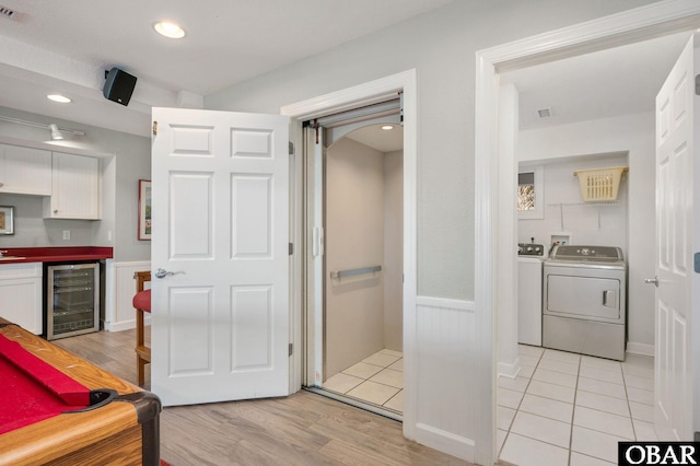 interior space featuring a wainscoted wall, wine cooler, white cabinetry, and separate washer and dryer