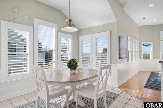 dining space with light tile patterned floors, wainscoting, lofted ceiling, and visible vents