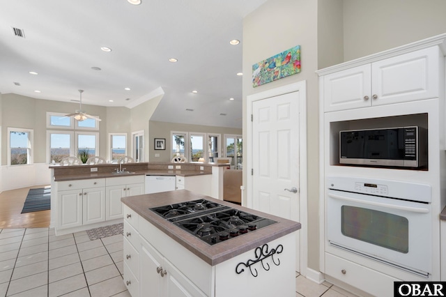 kitchen with a peninsula, white appliances, white cabinets, a center island, and dark countertops