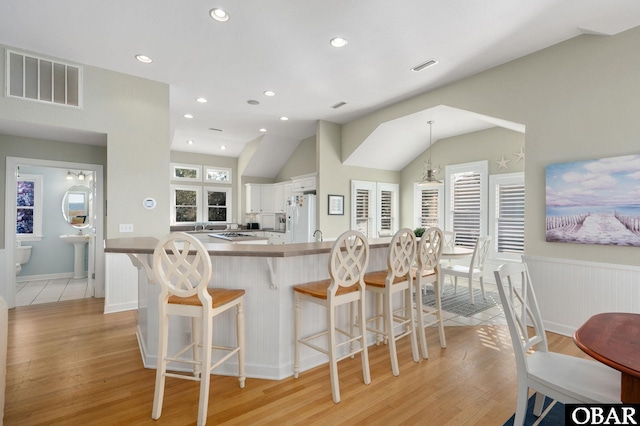 kitchen featuring visible vents, a kitchen breakfast bar, light wood-type flooring, white fridge with ice dispenser, and white cabinetry