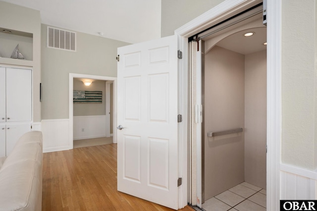 hallway featuring a wainscoted wall, light wood finished floors, arched walkways, and visible vents