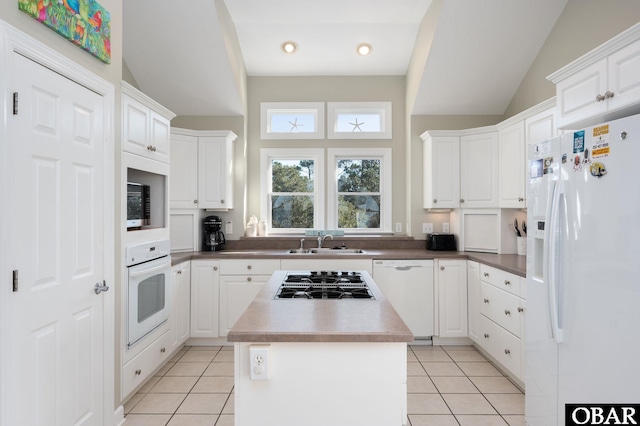 kitchen with white appliances, a kitchen island, white cabinets, and a sink