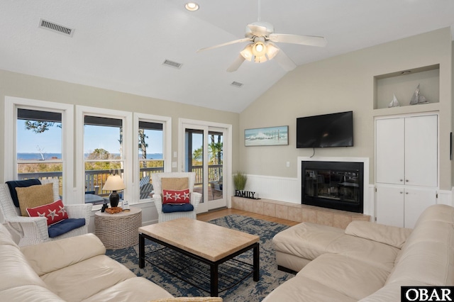 living room featuring visible vents, a tiled fireplace, light wood-style floors, wainscoting, and vaulted ceiling