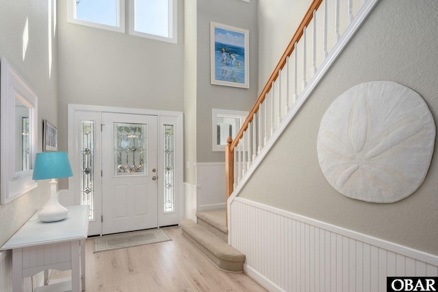 entryway with light wood-style floors, wainscoting, stairway, and a towering ceiling