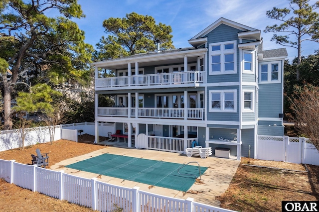 rear view of property featuring a balcony, a patio area, a fenced backyard, and a fenced in pool