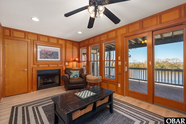 living area featuring ceiling fan, a water view, a fireplace, light wood-style floors, and crown molding