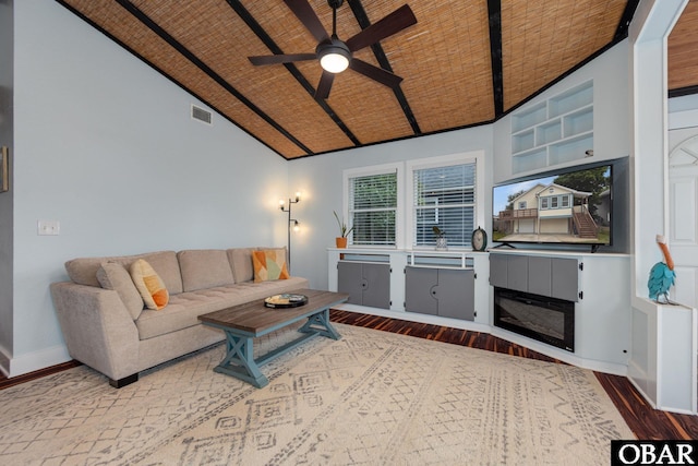 living area featuring dark wood finished floors, a ceiling fan, vaulted ceiling, a glass covered fireplace, and baseboards