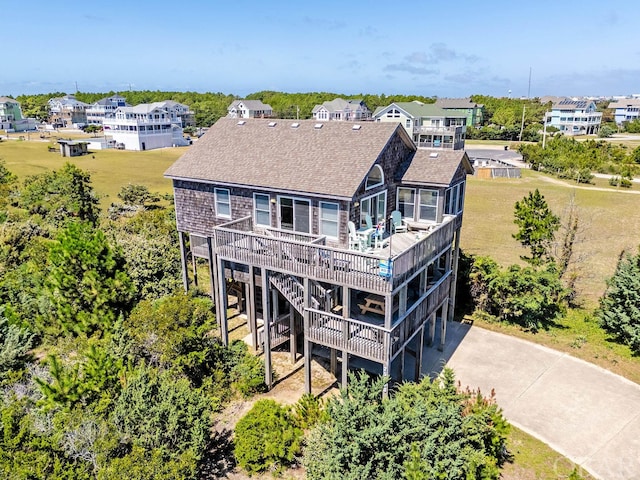 rear view of house featuring concrete driveway, stairway, roof with shingles, a wooden deck, and a residential view