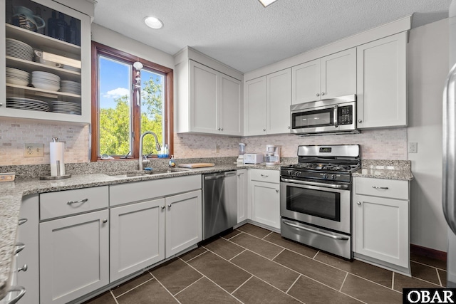 kitchen with stainless steel appliances, a sink, white cabinetry, decorative backsplash, and a textured ceiling