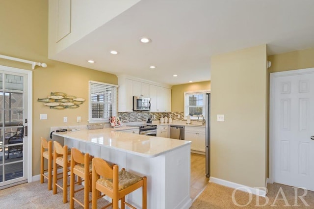 kitchen with white cabinets, a breakfast bar area, a peninsula, stainless steel appliances, and light countertops