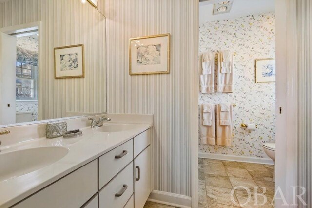 bathroom featuring double vanity, a sink, toilet, and wallpapered walls