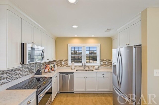 kitchen featuring light wood finished floors, decorative backsplash, appliances with stainless steel finishes, white cabinetry, and a sink