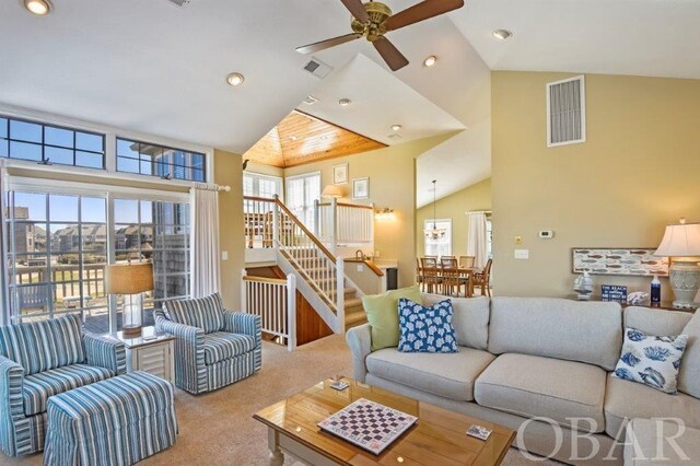 carpeted living area featuring high vaulted ceiling, stairway, visible vents, and a ceiling fan