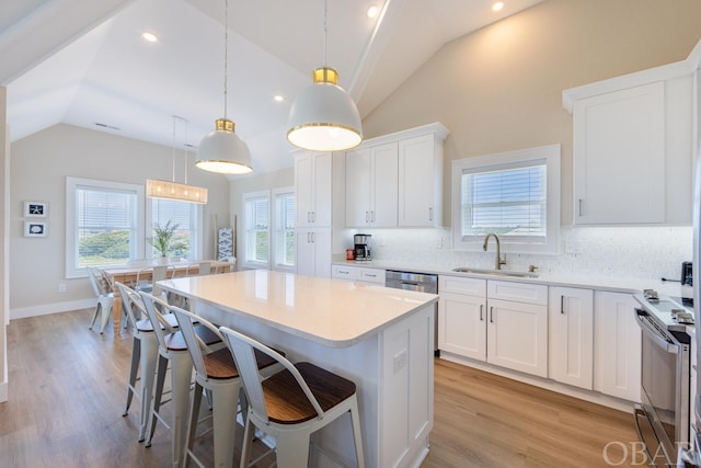 kitchen with a sink, white cabinets, light countertops, a kitchen bar, and pendant lighting