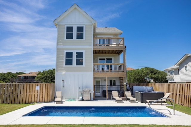 back of property with a hot tub, a patio, a balcony, a fenced backyard, and board and batten siding