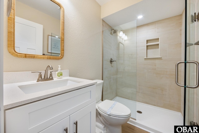 full bathroom featuring toilet, a textured wall, a tile shower, and vanity