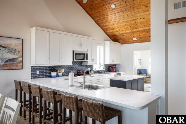 kitchen featuring a center island, light countertops, stainless steel microwave, white cabinetry, and a peninsula