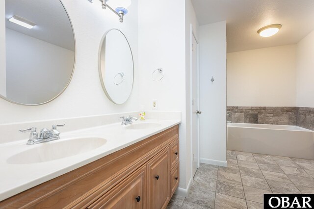 bathroom with a garden tub, double vanity, a sink, and baseboards