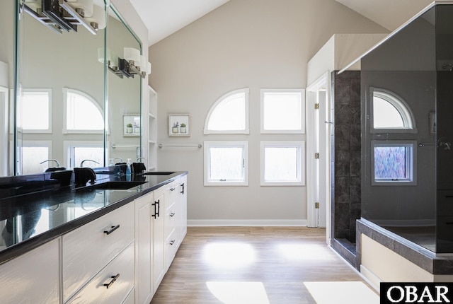 bathroom with wood finished floors, high vaulted ceiling, double vanity, and a tile shower