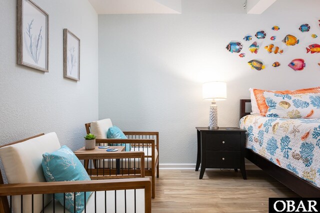 bedroom featuring light wood-style floors, a textured wall, and baseboards