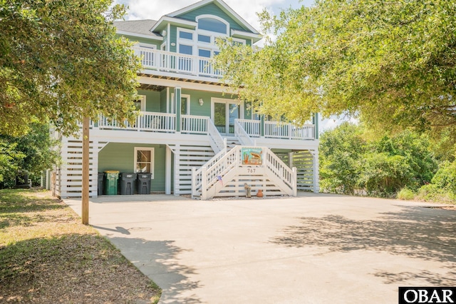 back of property featuring covered porch, roof with shingles, stairs, driveway, and a carport