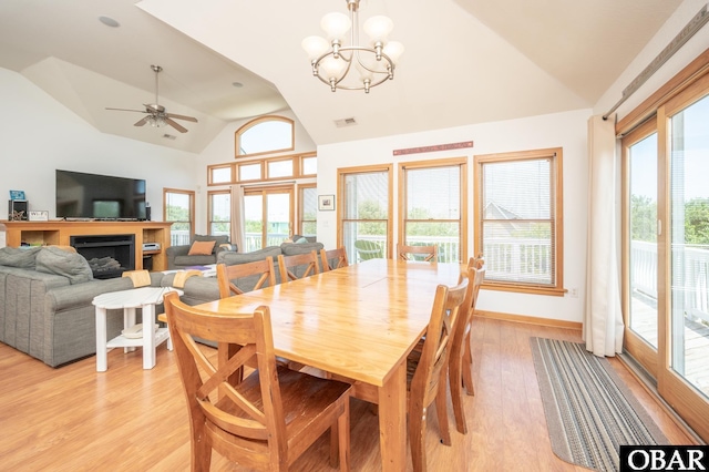 dining space with visible vents, a fireplace, light wood-style flooring, ceiling fan with notable chandelier, and vaulted ceiling