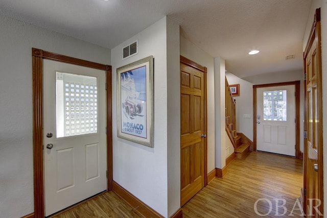 foyer featuring stairs, light wood-type flooring, visible vents, and baseboards