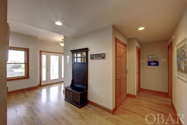 foyer with light wood-style flooring, visible vents, and baseboards